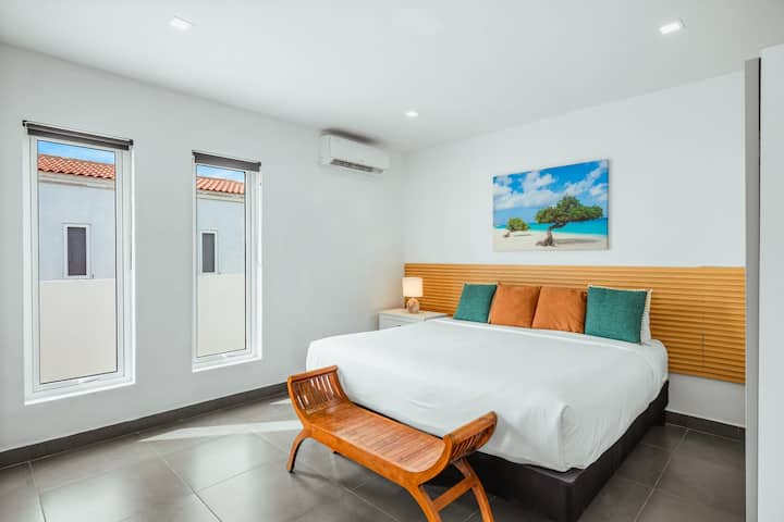 Tranquilo dormitorio con cama tamaño king, obras de arte tropicales, detalles en madera cálida y cojines de colores vivos