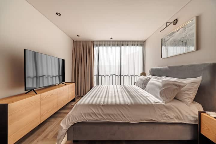 Habitación moderna y espaciosa con cama tamaño queen, grandes ventanales con hermosas vistas, gran luz natural y televisor. Perfecto para relajarse con comodidad y estilo.