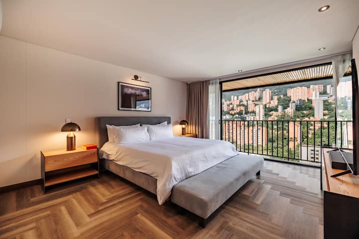 Elegante dormitorio principal con cama tamaño king, impresionantes vistas y abundante luz natural. Relájate con estilo mientras disfrutas de una habitación espaciosa y luminosa con un televisor grande.