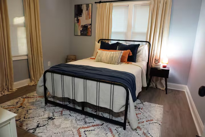 חדר שינה נעים עם מצעים שכבתיים בצבע כחול כהה וניטרלי, וילונות רכים ותאורת לילה חמימה. המיטה ממוקמת במרכז לנוחות, עם גישה נוחה לשידות לילה ומקום רגוע להירגע בו.
