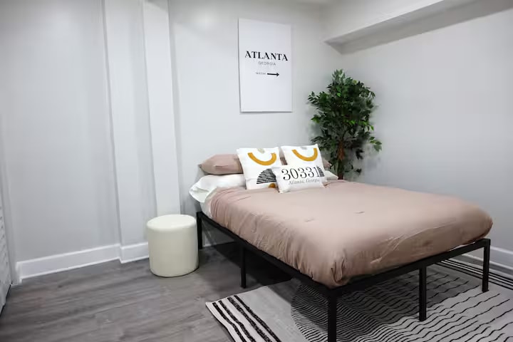 חדר שינה רך וניטרלי עם מצעים מרובדים, יצירות אמנות פשוטות ותחושה רגועה ולא עמוסה. המיטה מעוצבת למנוחה, עם שטח רצפה פתוח שמאפשר להתמקם בקלות בחדר.