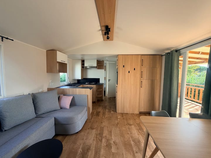 Dhomë ndenjjeje e këndshme dhe e ndritshme me divan të madh, televizor dhe ambient të brendshëm ngrënieje me pamje nga një tarracë e madhe prej druri me pamje nga liqeni