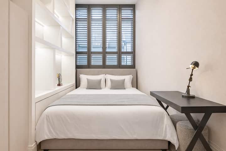 Një dhomë gjumi e mobiluar bukur me një krevat dopio luksoz, rafte të ndriçuara me porosi, grila të përshtatura dhe një tavolinë shkrimi elegante, duke krijuar një vend të qetë dhe të rafinuar me luks të nënvlerësuar.