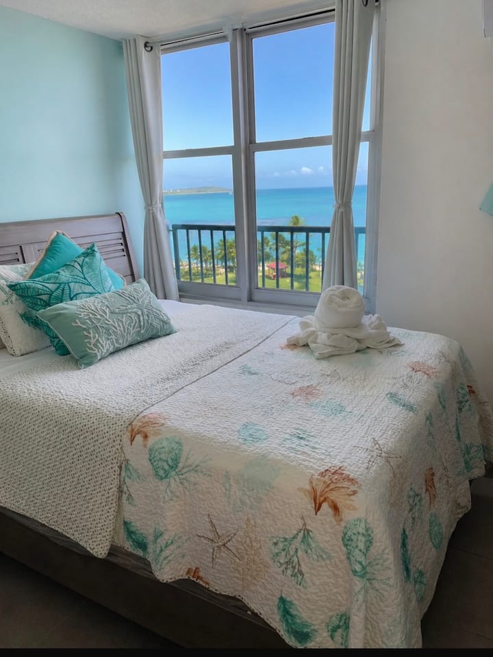 Comfortable bed next to large windows overlooking the ocean. A bright and quiet space to relax during your stay.