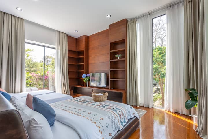 Suite familiale spacieuse à Chiang Mai avec lits jumeaux et vue sur le jardin. Chambre moderne dans une villa, avec une décoration en bois chaleureuse, de la lumière naturelle et un grand espace au sol. Havre de paix sûr et calme pour les familles et les vacances multigénérationnelles en Thaïlande.