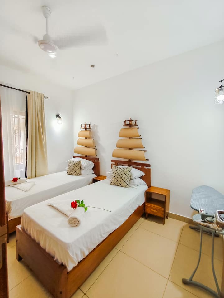 Спална соба инспирирана од крајбрежјето со смирувачки тонови и удобни кревети за мирен сон. 