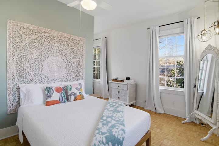 Quarto queen com cama aconchegante, janelas altas, espelho de corpo inteiro e cômoda.