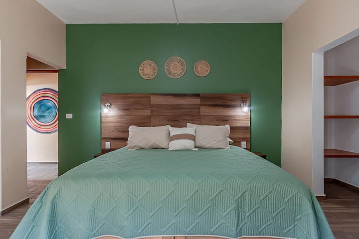 Detalle de la cama King Size en la recámara principal, con cabecera apariencia de madera y decoración cálida que crea un ambiente acogedor y relajante.