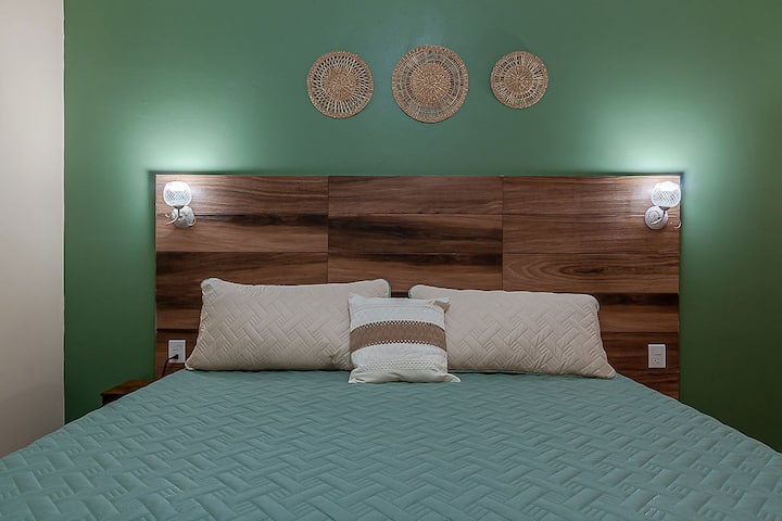 Detalle de la cama King Size con cabecera apariencia de madera y decoración cálida, creando un ambiente acogedor y confortable para el descanso.