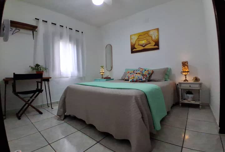 Suíte 1 aconchegante e iluminada, com cama queen e cama auxiliar, ideal para casais ou pequenas famílias. Ambiente leve, decoração acolhedora, luz natural e clima tranquilo para descansar após um dia de praia e natureza na Casa Amélia.