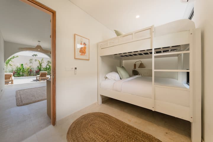 Fun bunk bedroom with white wooden bunk beds dressed in crisp white sheets and green pillows. Direct garden access and views of the swimming pool with sun loungers make this room perfect for families or groups staying in Amed.