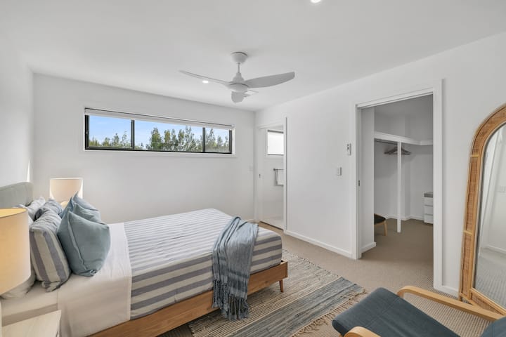The main bedroom features a comfortable queen-sized bed and a spacious walk-in wardrobe. The ensuite offers a large, modern shower. A cot is also provided and stored in the walk-in wardrobe.