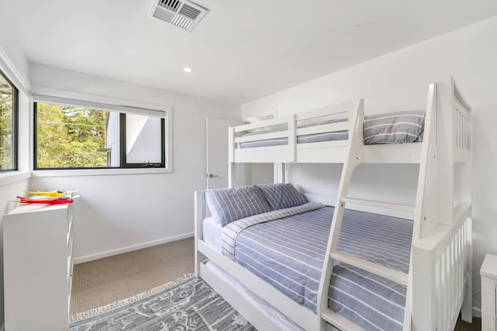 Bedroom three is a flexible family-friendly space featuring a tri-bunk (single over double) plus a slide-out trundle bed, ideal for groups or children. Fresh linen and towels are provided.