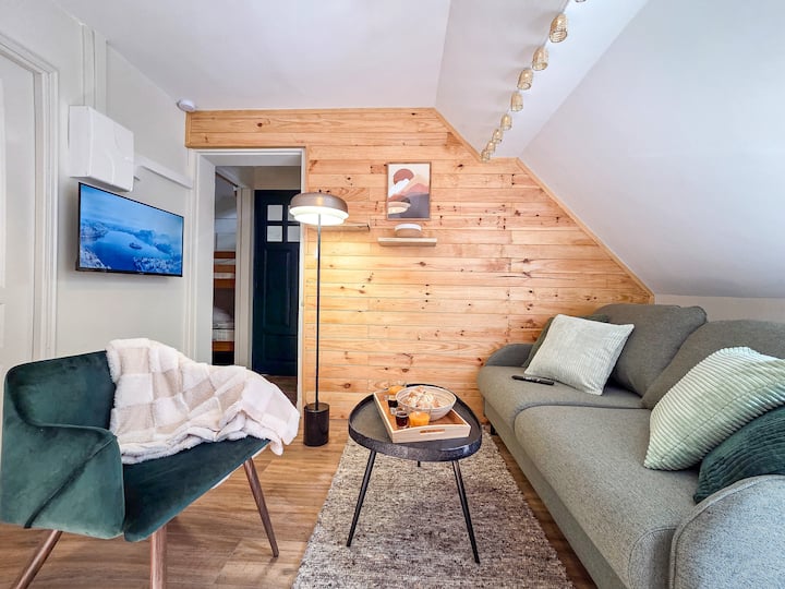 Cómoda sala de estar, con un sofá de dos plazas convertible y un sillón que invita a la relajación. Una pequeña mesa de centro permite colocar libros o bebidas, y la televisión conectada a la pared completa este espacio ideal para relajarse.