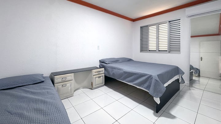 Quarto com ar-condicionado, uma cama de solteiro e uma cama de casal, com roupas de cama e travesseiros inclusos.