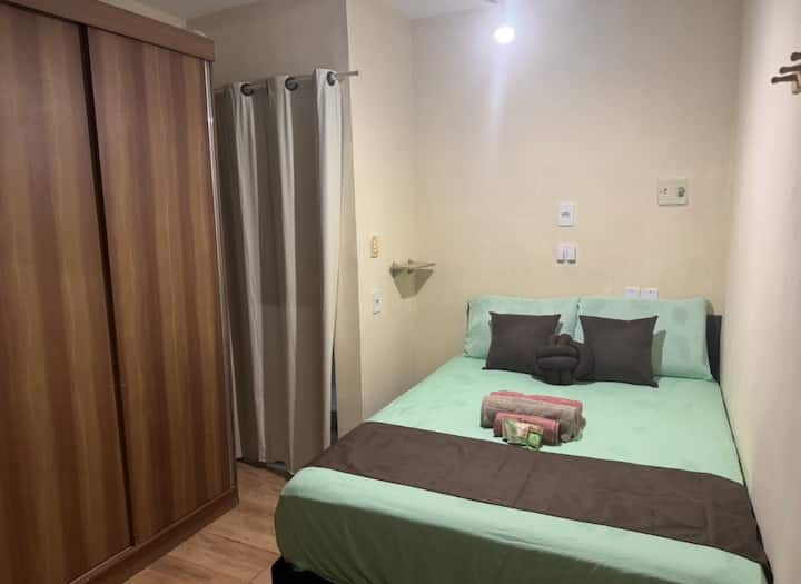 Chambre avec lit double, ventilateur de plafond, armoire, rideau occultant, cintres et climatisation.