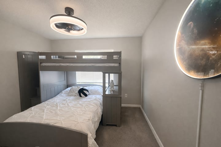 Divertida habitación inspirada en el espacio con una litera inferior doble y una litera superior individual para dormir de forma flexible.