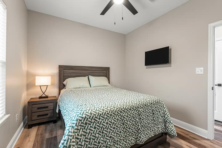 Relájate en este acogedor dormitorio, bañado por la suave luz de las persianas. Disfruta de una cómoda cama tamaño queen y entretenimiento en el televisor montado en la pared. Perfecto para parejas o familias que buscan un refugio relajante.