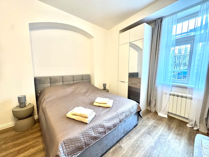 Habitación acogedora con una cómoda cama matrimonial tapizada de 160 × 200 cm, lámparas y mesitas de noche, y un ropero con espejo. Luminosa y perfecta para un sueño reparador