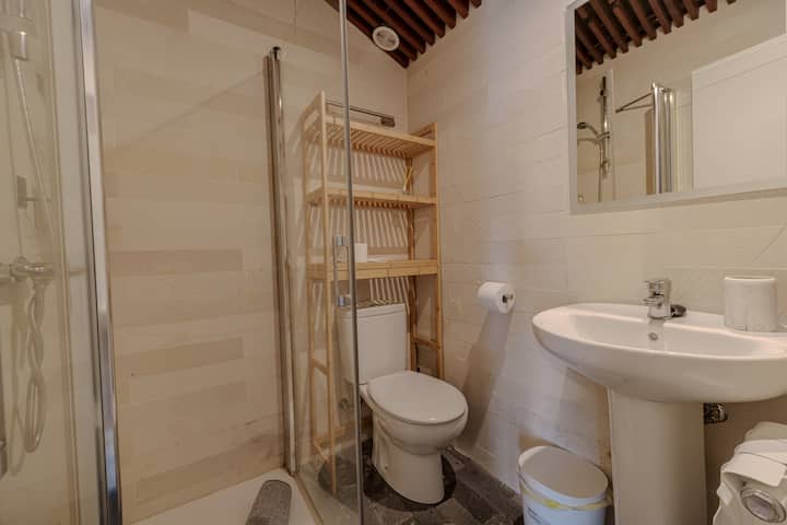 Baño completo con ducha y repisas de madera.