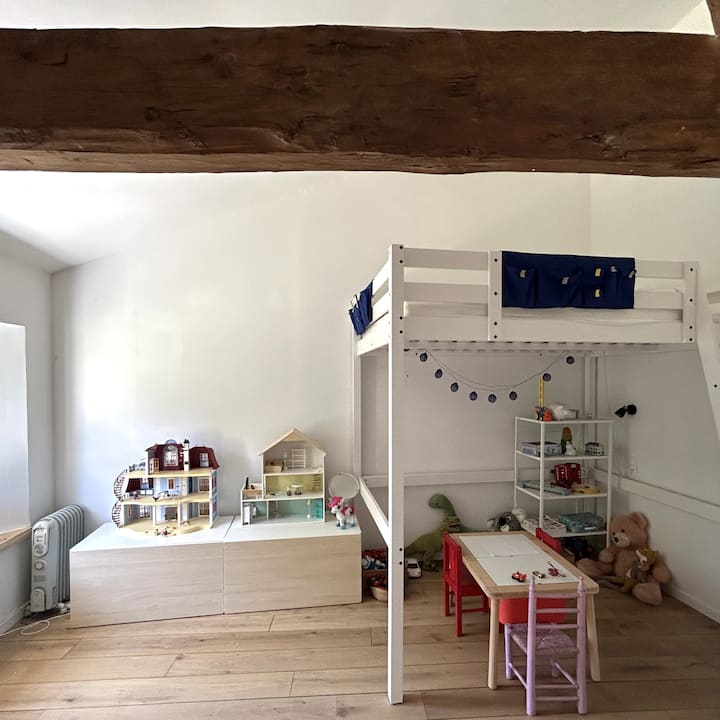 Habitación infantil con diversos juegos tanto para niños como para niñas, con una cama doble en el altillo.