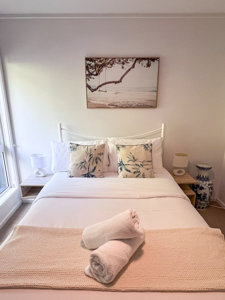 Tranquila habitación doble con suave luz natural, armario para guardar ropa y serenas obras de arte costeras
