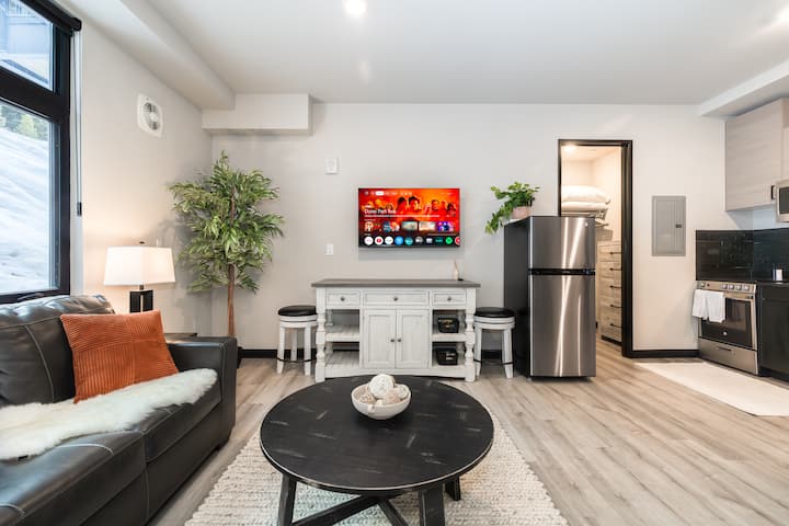 Unwind with a comfortable living room. Features a leather sofa for two with cozy blankets, views of the slope through the primary windows, access to the smart TV for your favorite streaming, and large table for eating, working, or cook prep.