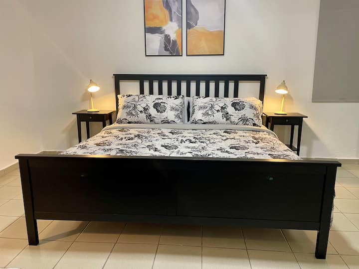 “Habitación grande y luminosa con una cama tamaño king y una tamaño queen, que ofrece mucho espacio y comodidad. Cuenta con una moderna decoración en blanco y negro, ventilador de techo, aire acondicionado, persianas opacas, mesitas de noche con lámparas y un diseño limpio y elegante, ideal para familias o grupos”.