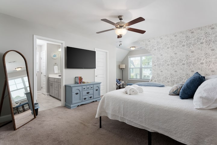 Suite luminosa con cama king, televisor, baño privado y detalles elegantes