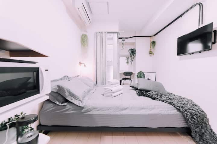 Cama matrimonial con sábanas y toallas grises, con un televisor enfrente