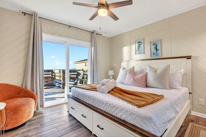 Despiértese con vistas al mar desde su terraza privada en este luminoso dormitorio de estilo playero, con paredes de tablas superpuestas y un acogedor rincón de lectura.