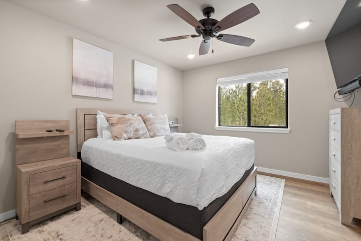 พักผ่อนในห้องพักกว้างขวางพร้อมเครื่องนอนสีขาวนุ่มๆ งานศิลปะในกรอบ และหน้าต่างบานใหญ่ที่มองเห็นต้นไม้