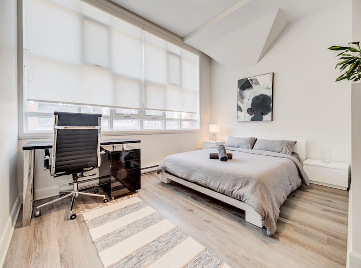 Minimalistická spálňa v Montreale so sivou posteľnou bielizňou, útulným pracovným priestorom pri okne a elegantným moderným štýlom.