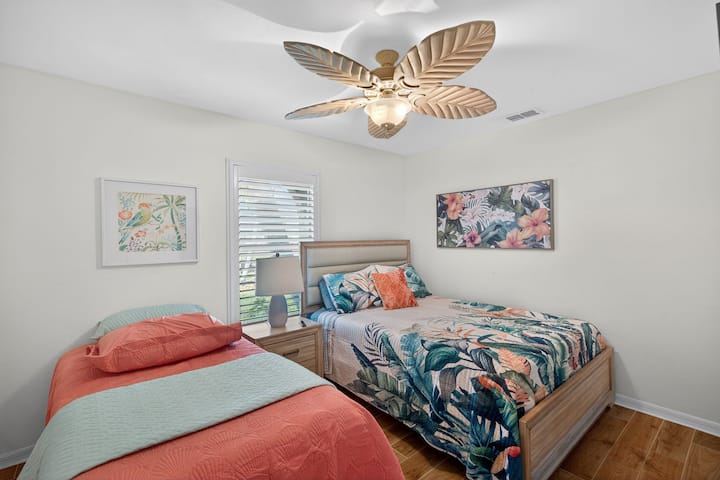 חדר שינה לאורחים הכולל מיטת קווין סייז ומיטת יחיד, מאוורר תקרה ועיצוב חוף בהיר - מושלם לילדים או לאורחים נוספים.