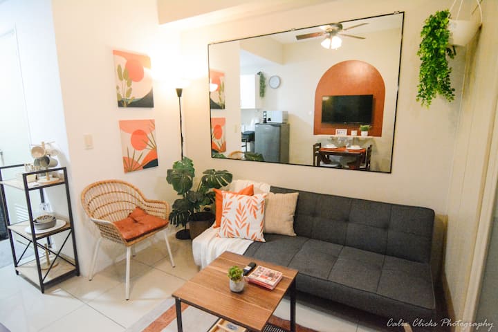 Step into a cozy, soft-modern living space designed for comfort and style. The unit features clean white interiors accented with warm orange tones and touches of greenery, creating a relaxing and homey atmosphere.