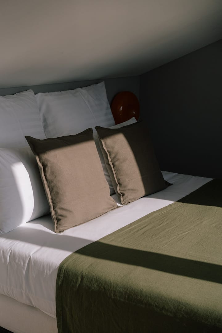 Udoban krevet ispod nagnutog stropa s mekanim jastucima i toplim prirodnim svjetlom koje prodire u prostoriju