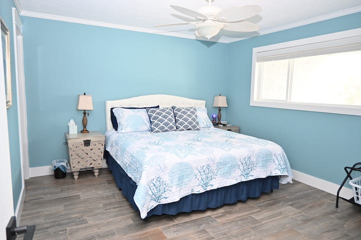 Спална соба со брачен кревет (king size) на главното ниво со ноќни масички од секоја страна и светилки. 