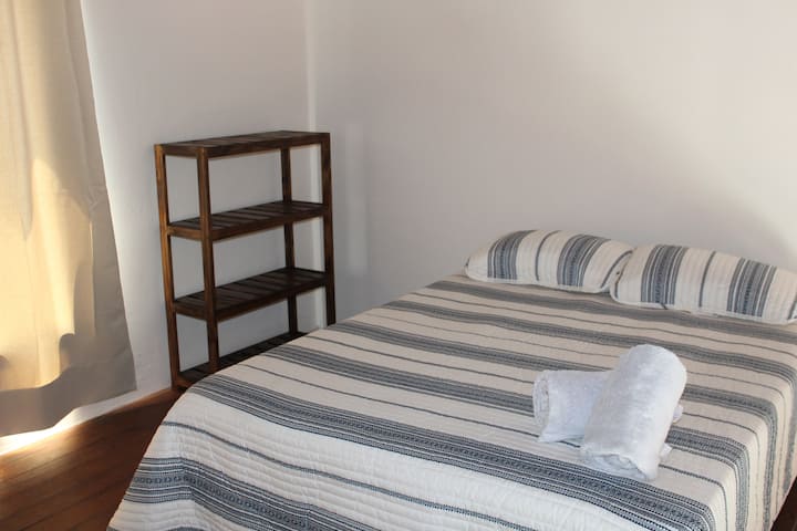Recámara con estante de madera para ropa y otras pertenencias y cama con ropa completa.