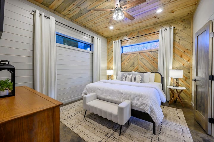 Este moderno dormitorio de cabaña cuenta con techos altos de madera, una cama con dosel y paredes con ventanas que ofrecen vistas a la montaña.