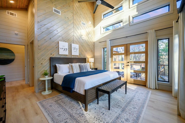 Este hermoso dormitorio principal cuenta con techos altos, tragaluces y acceso directo a una terraza al aire libre con vista a los árboles.