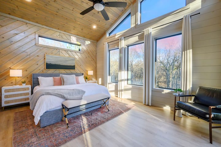 Despiértese con ventanas del piso al techo y un techo abovedado de madera en este impresionante y moderno dormitorio.