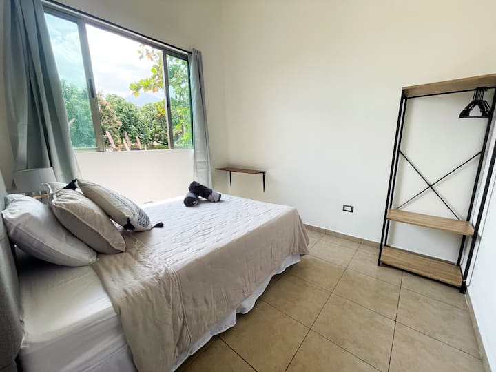 Recámara amplia y acogedora con cama matrimonial y suaves sábanas de algodón. Cuenta con ventana que brinda luz natural y vista fresca. Incluye cortinas blackout para mayor confort y descanso, además de un práctico perchero para organizar tu ropa.