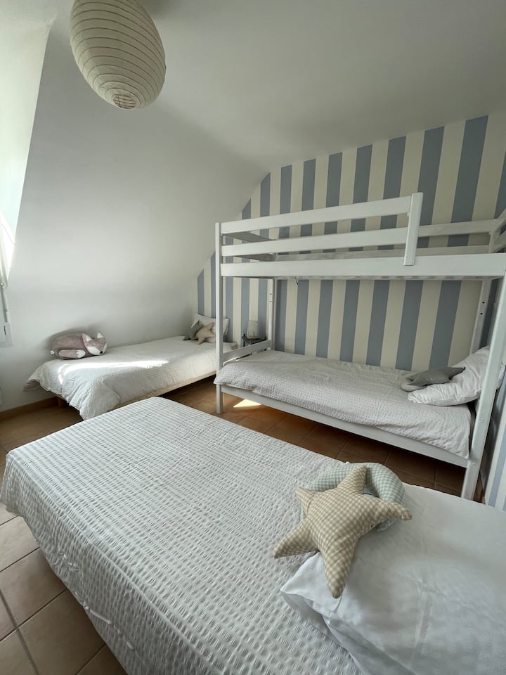 Dormitorio compuesto por dos camas individuales y una litera, cómoda con cajones, zona de biblioteca y juegos.
