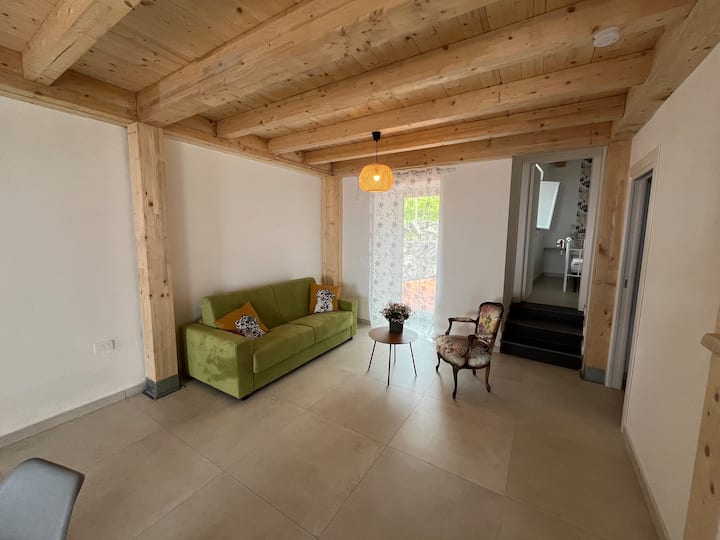 Blick in den hinteren Teil des Wohn-Essbereichs mit Schlafcouch, Zugang zu Badezimmer, Schlafzimmer und Zugang zum hinteren Terrassenbereich.