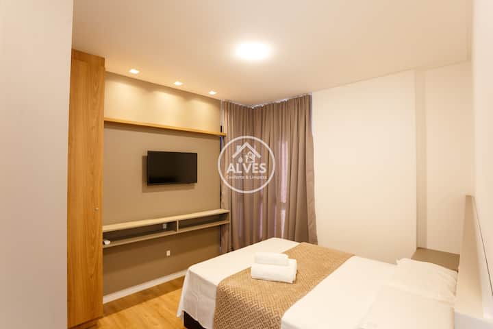 O quarto oferece uma cama de casal aconchegante com suíte e armazenamento com guarda-roupas sob medida. O design clean, com mesas de cabeceira flutuantes e iluminação suave, cria o refúgio perfeito para relaxar após um dia de passeios ou trabalho.