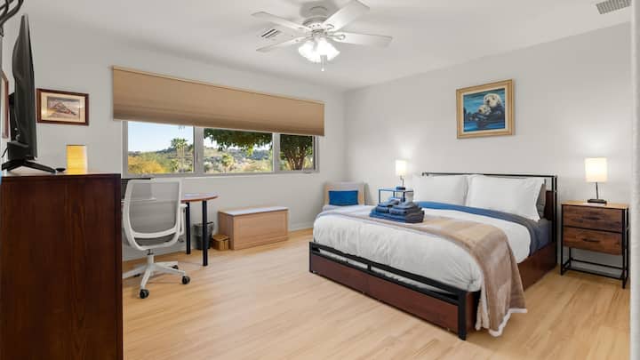 Spacious master bedroom featuring a comfortable bed, Smart TV, dedicated workspace, and scenic desert views—designed for both restful nights and productive mornings.