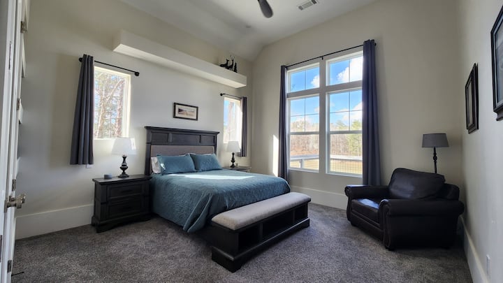 Disfruta de la comodidad en este dormitorio en el piso principal, que cuenta con una lujosa cama tamaño queen. Desempaca con facilidad gracias a los estantes empotrados y al espacioso armario. Disfruta de momentos de tranquilidad en el cómodo sillón de cuero con vistas a las copas de los árboles y al agua a través de las ventanas.