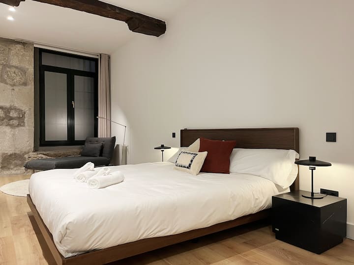 Dormitorio principal con cama doble y chaise longue junto a la ventana.