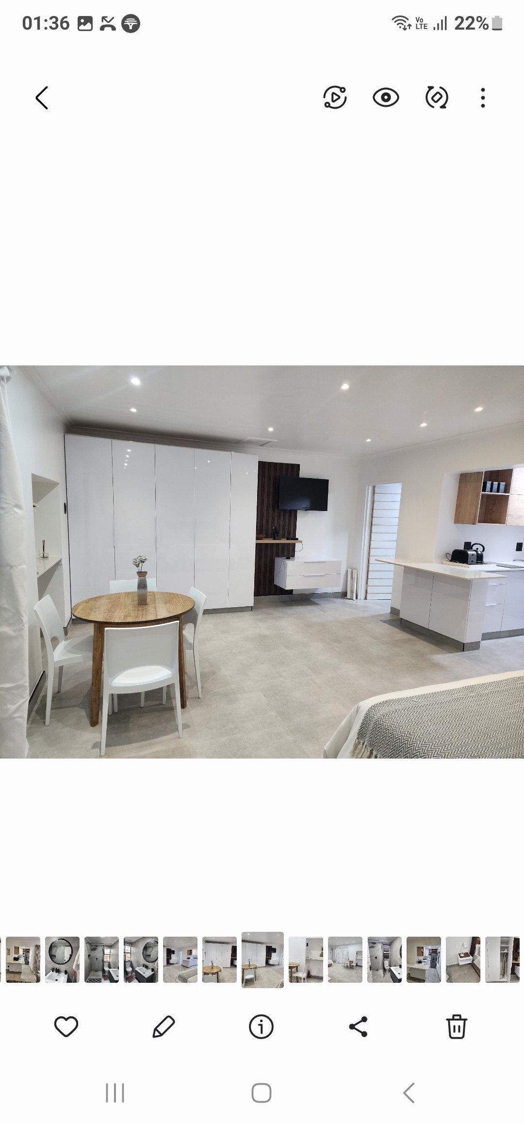 An open plan studio unit is presented, featuring light-colored walls and modern furnishings. A round table with two chairs is positioned near the kitchenette, where sleek cabinetry is visible alongside a small television. The cozy sleeping area is discernible, with natural light brightening the space.