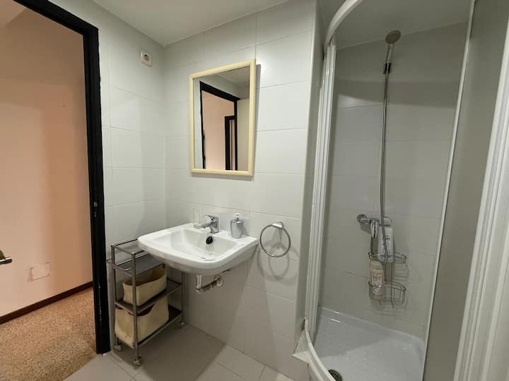 Baño con lavabo, espejo y ducha de plato blanco.